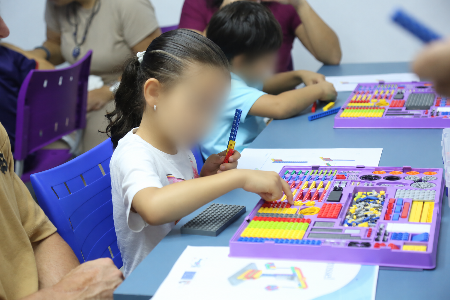 Crianças explorando peças de robótica em aula, com rostos desfocados